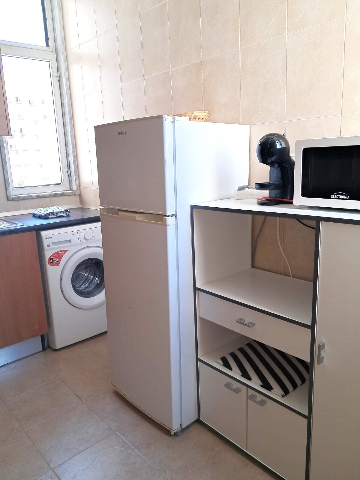 A compact kitchen with a washing machine, a refrigerator, and a microwave.