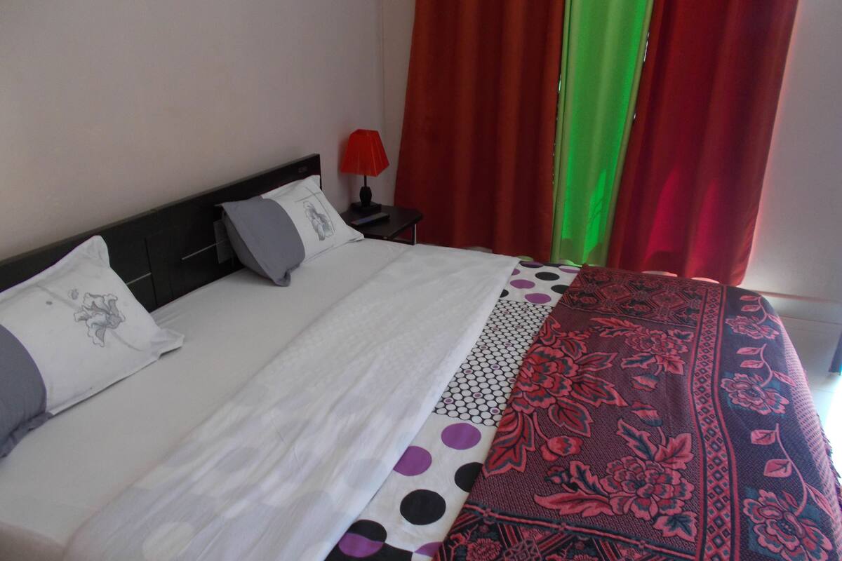 A neatly made bed with a white and black polka dot bedspread, a red and black floral blanket, and a gray pillow with a floral design.