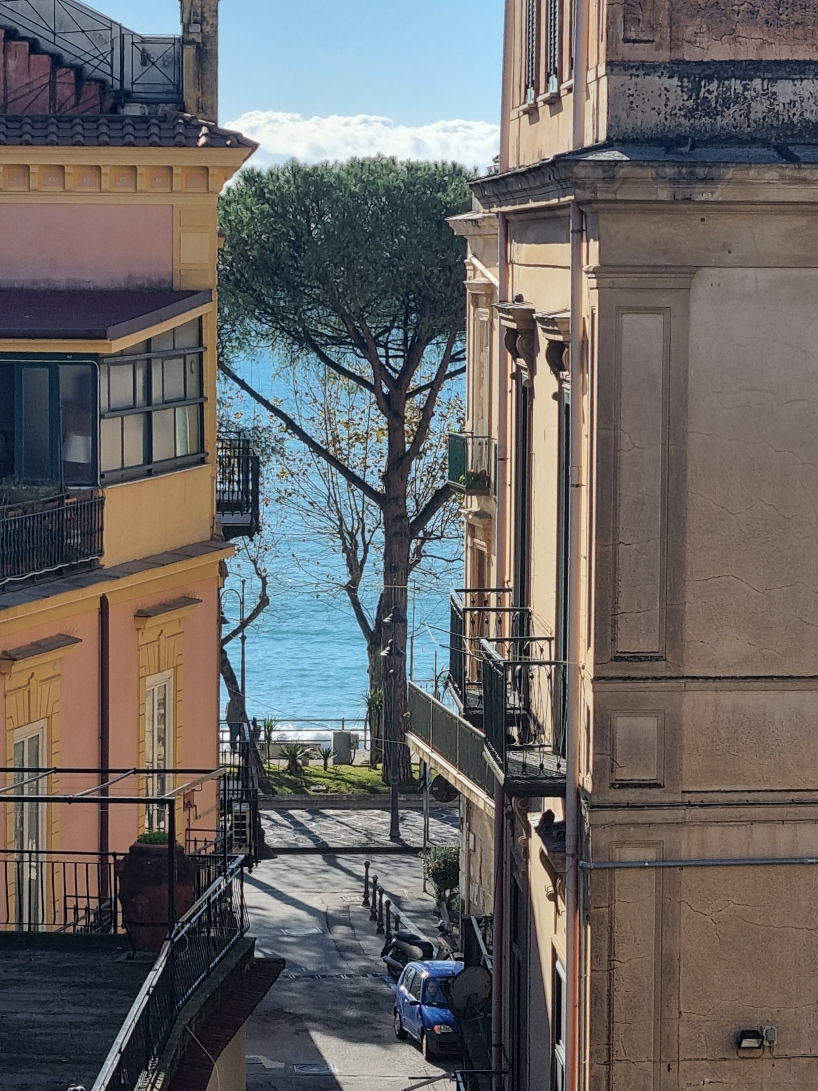 Un vicolo stretto con edifici su entrambi i lati, un albero al centro e vista sul mare sullo sfondo.