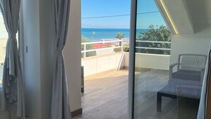 A balcony with a view of the sea, a chair, and a table.