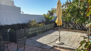 Eine Holzterrasse mit einem Metallstuhl und einem gelben Sonnenschirm.