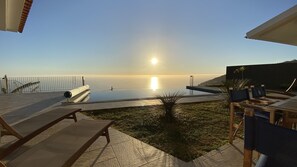 Ein Poolbereich mit Blick auf das Meer, eine Liege und ein Tisch.