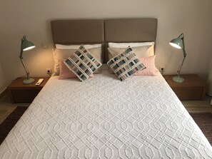 Ein ordentlich bezogenes Bett mit einer gemusterten Tagesdecke, zwei Nachttischlampen und zwei Zierkissen.