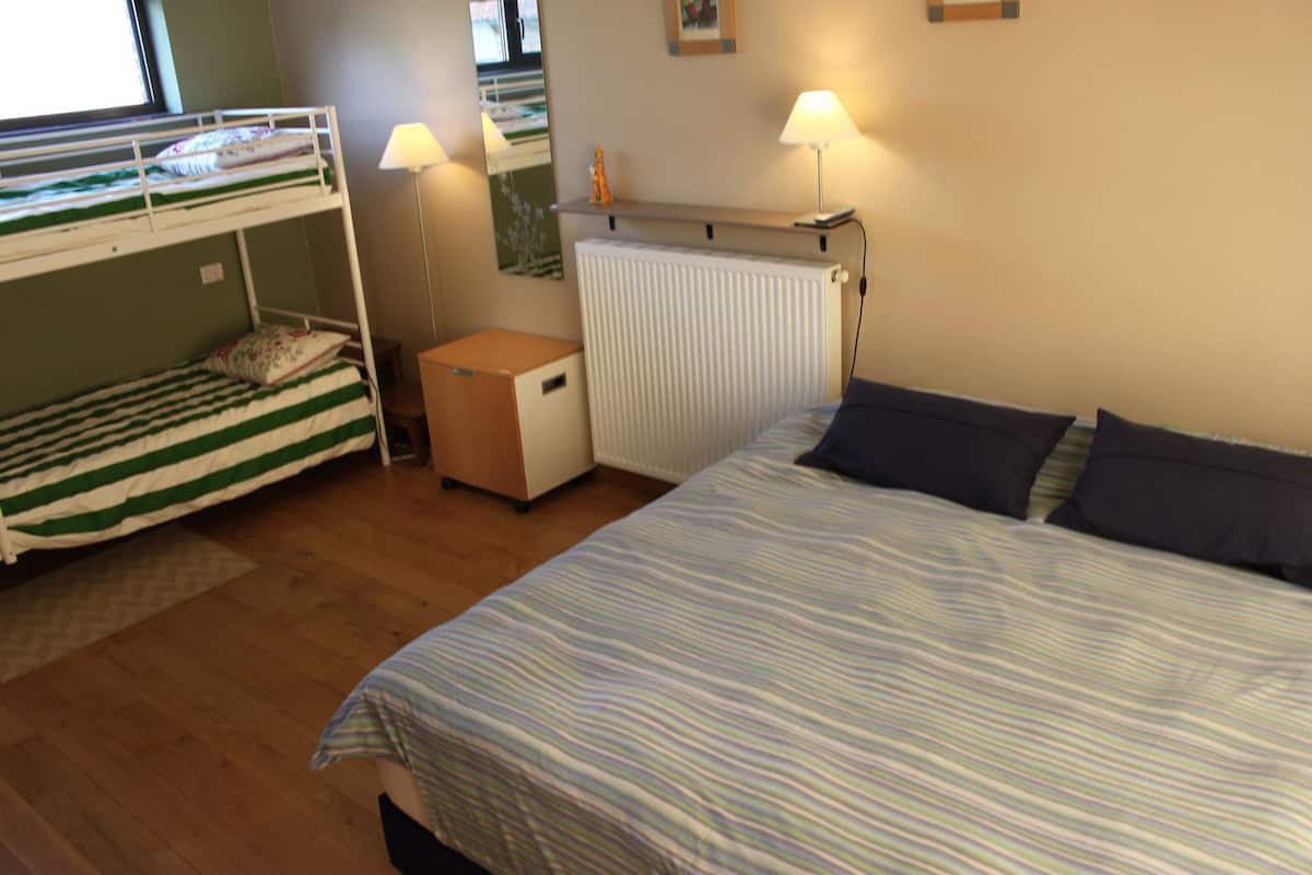 A room with bunk beds, a single bed, a radiator, a small cabinet, and two bedside lamps.