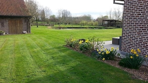 A well-maintained lawn with a brick building, a wooden structure, and a garden with yellow flowers. - Lomolen B&B (Aalter)