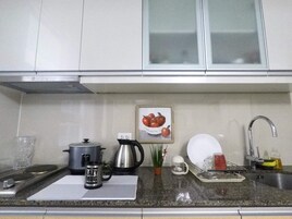 A kitchen with white cabinets, a stainless steel kettle, a coffee maker, a potted plant, and a framed picture of apples.