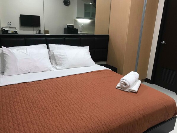 A hotel room with a bed, white pillows, a brown quilted bedspread, a folded towel, a flat-screen TV, a clock, and a mirror. - 101 Newport Condo Across the Airport (Pasay)