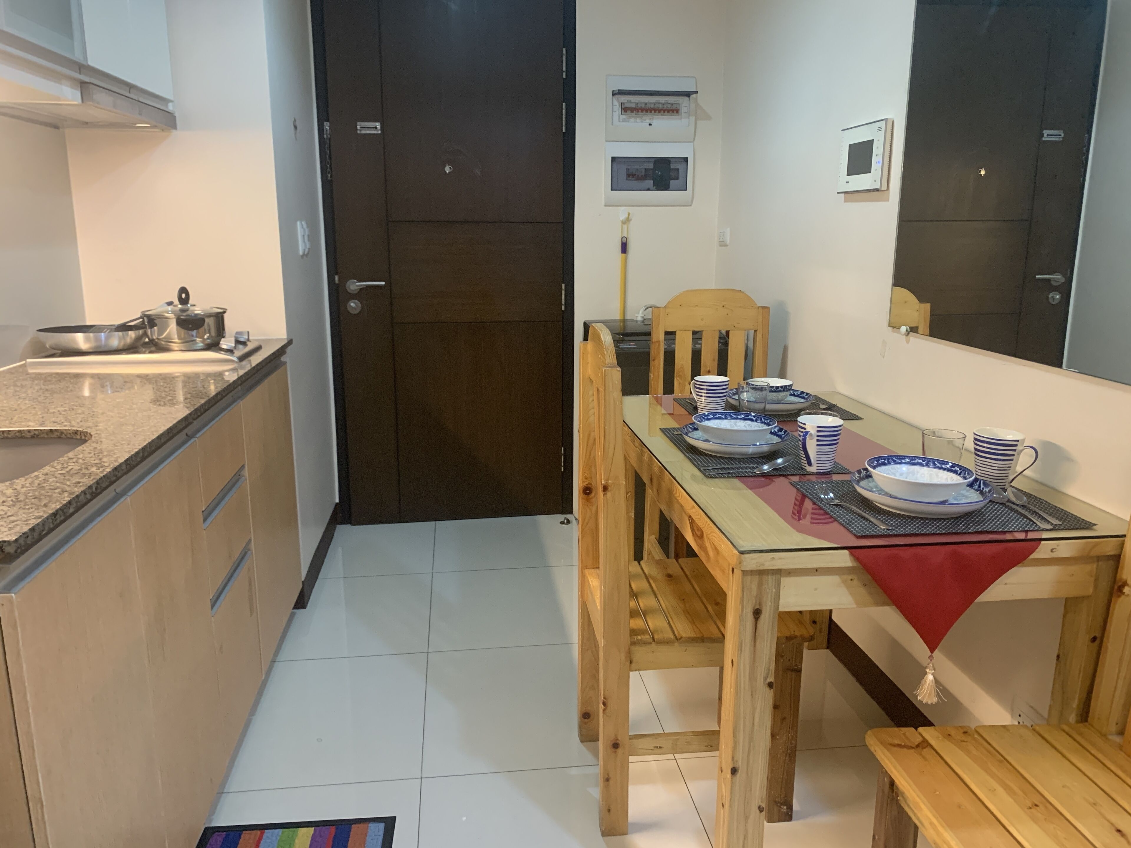 Una cocina compacta con zona de comedor, una mesa de madera dispuesta con platos y tazas, y un mantel rojo.