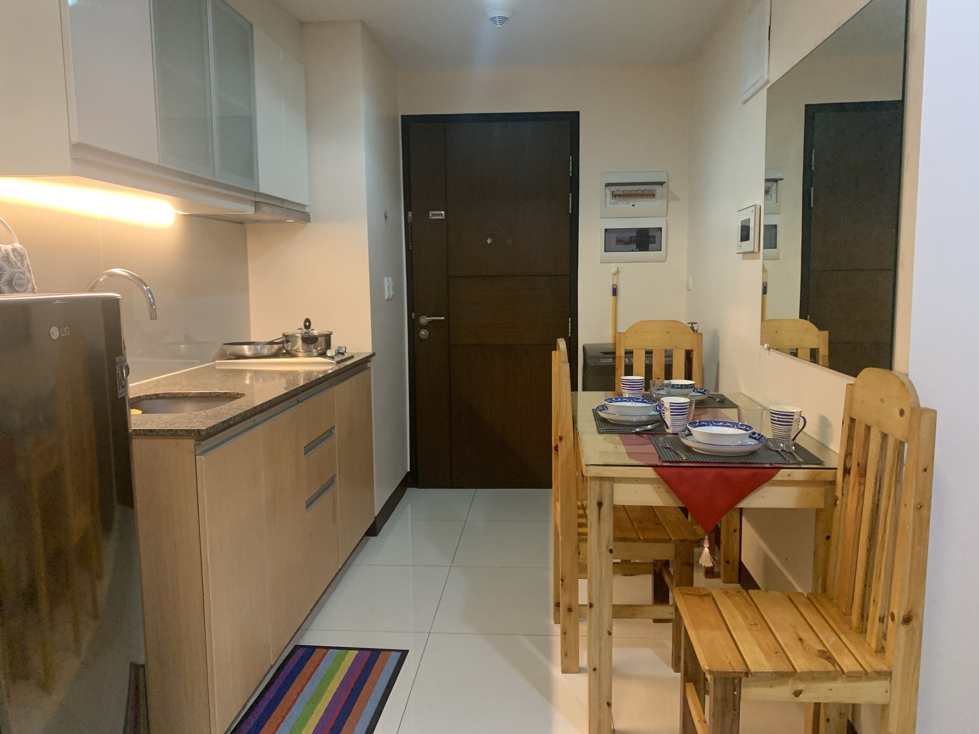 A compact kitchen with a refrigerator, sink, and cabinets. A dining table with chairs is set up in the center.