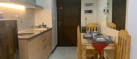 A compact kitchen with a refrigerator, sink, and cabinets. A dining table with chairs is set up in the center.