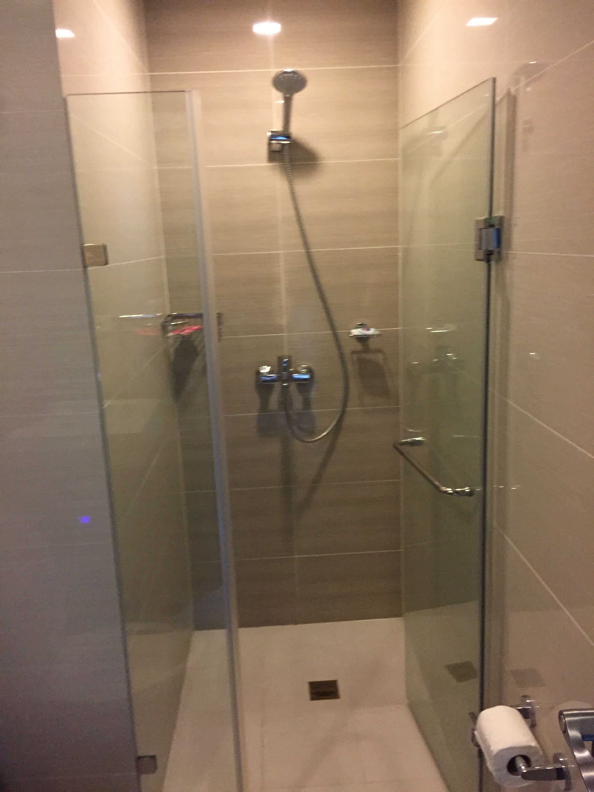 A glass-enclosed shower stall with a handheld showerhead and a wall-mounted faucet.