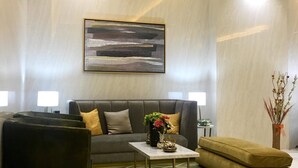 Una sala de estar moderna con un sofá gris, una mesita con un jarrón de flores y un otoman verde.