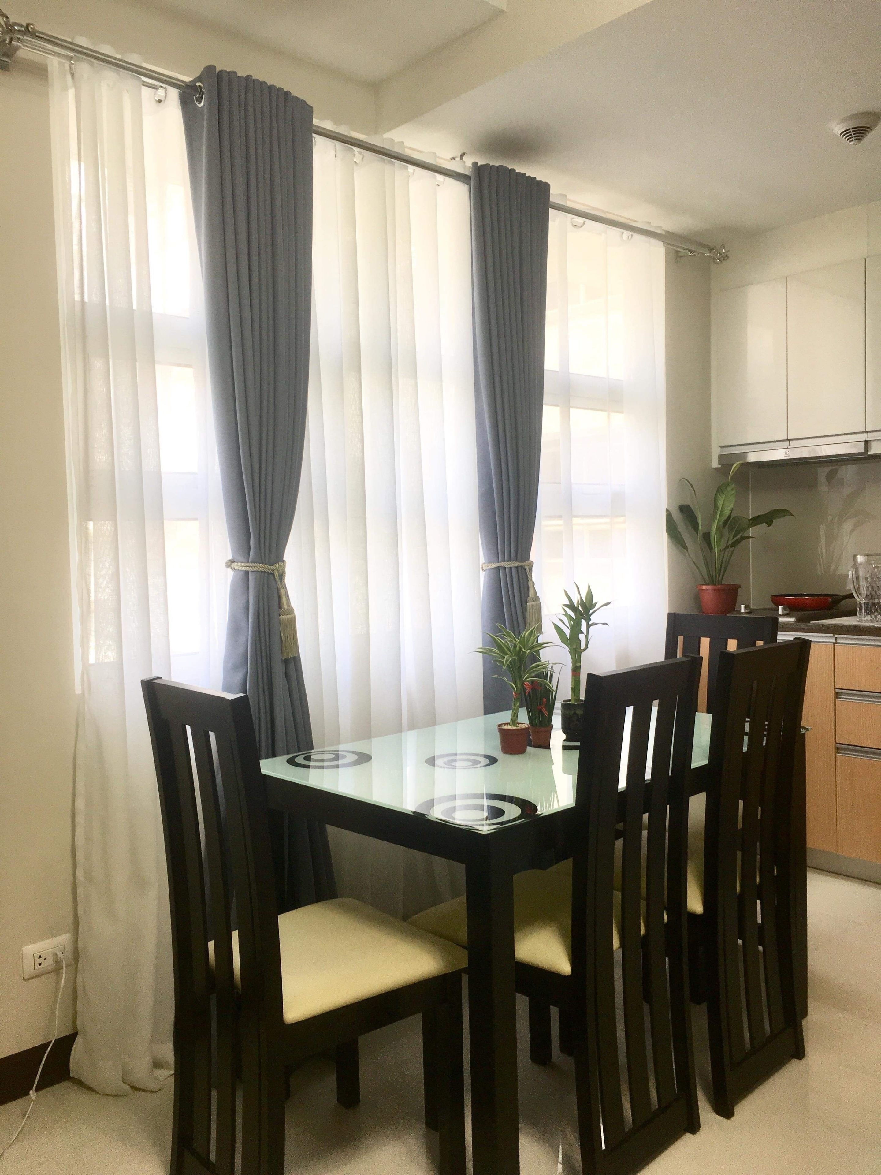 A dining area with a glass table, four chairs, and two potted plants.