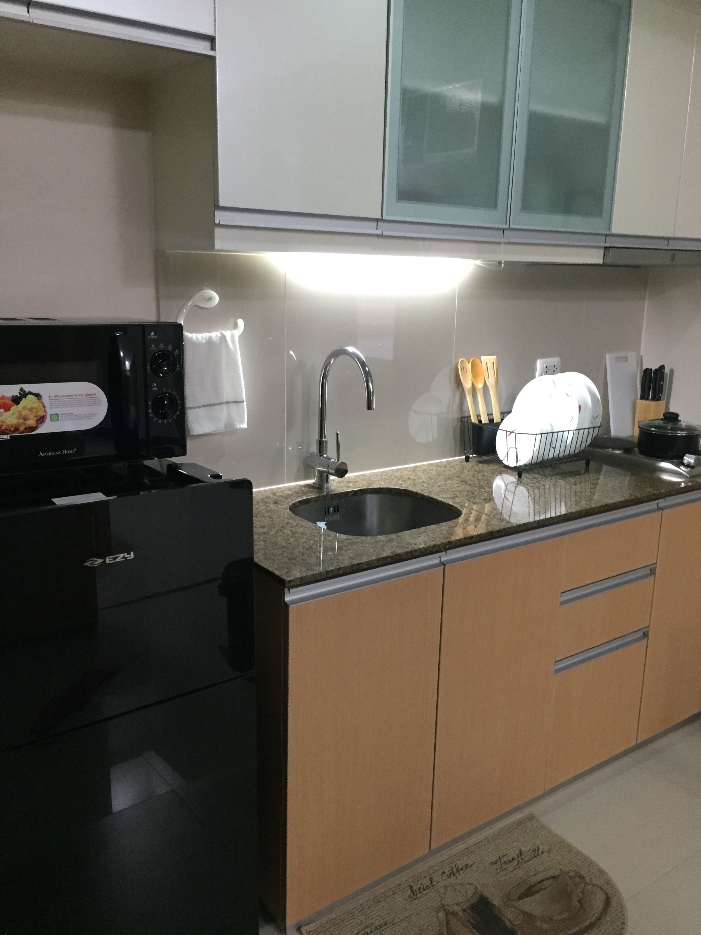 Una cocina con un refrigerador negro, un fregadero y alacenas.