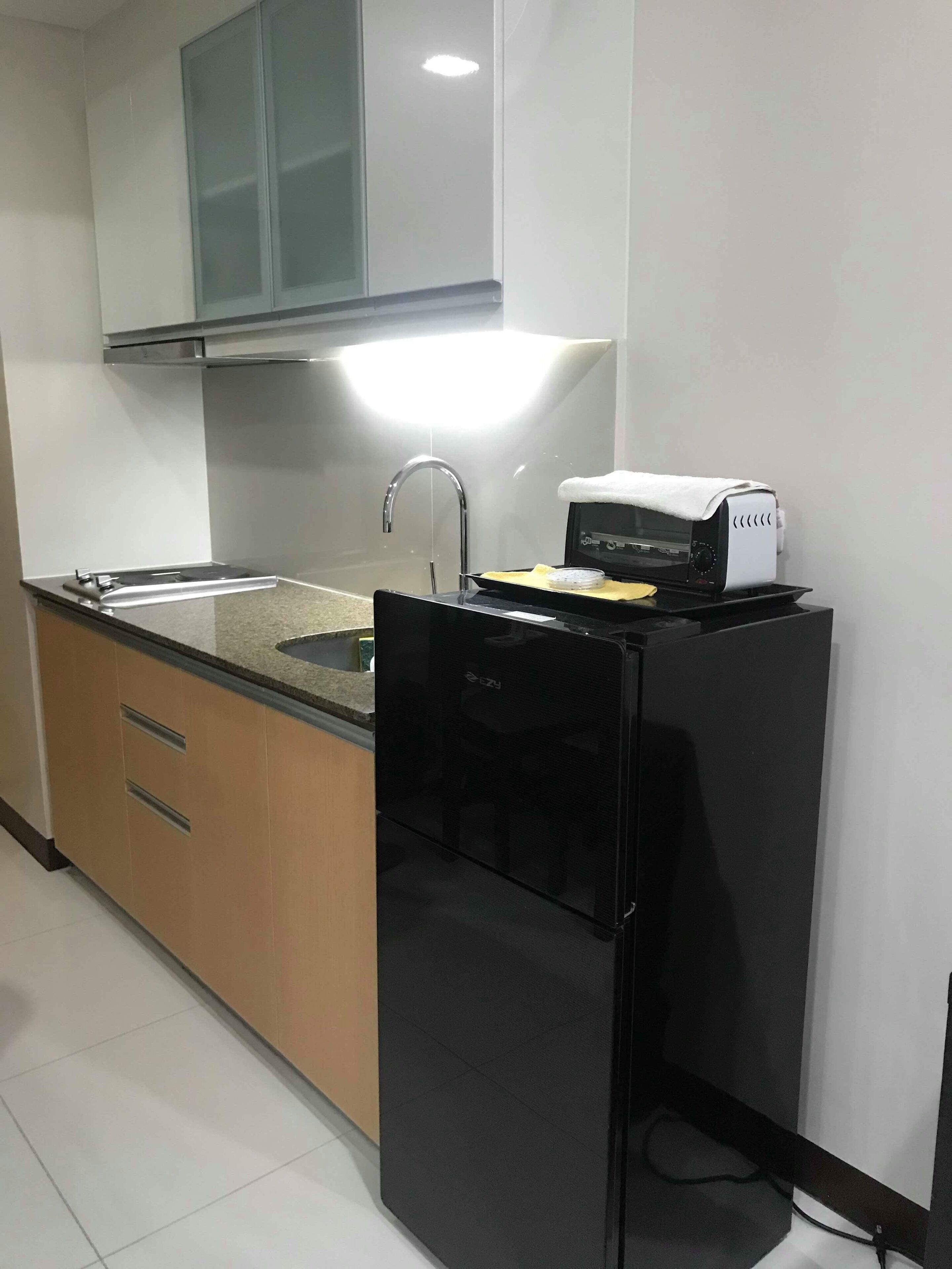 A compact kitchen with a black refrigerator, a built-in oven, a stainless steel sink, and wooden cabinets.