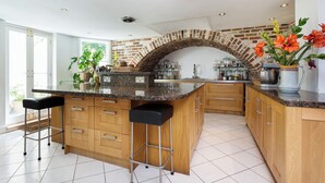 Uma cozinha com arco de tijolos, armários de madeira, bancada de granito e dois banquetas.