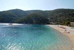 A beach with clear turquoise water, a sandy shore, and a backdrop of green hills.