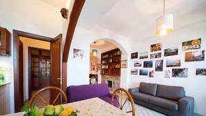 A cozy living area with a dining table set with lemons, a purple sofa, a grey sofa, and a bookshelf filled with books and framed photos. - Barabba sea house (Santa Teresa di Riva)