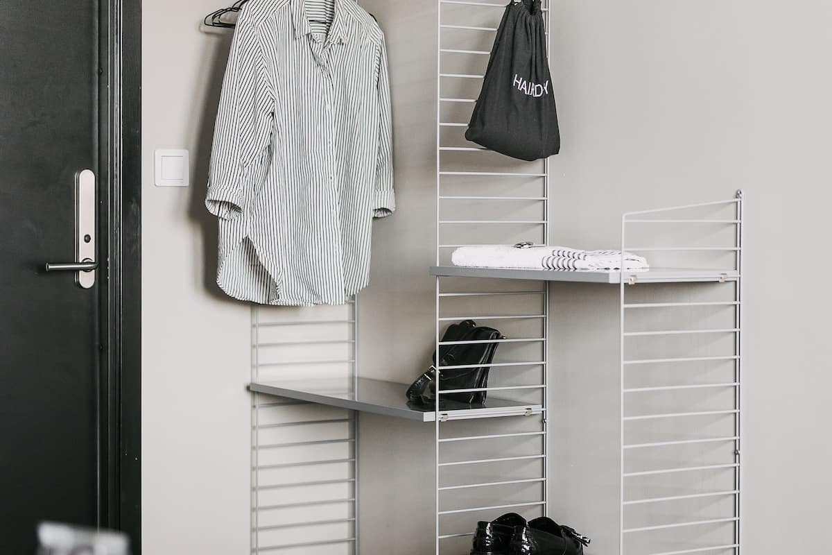 A room with a black door, a white wall, and a metal shelving unit with clothes and shoes.