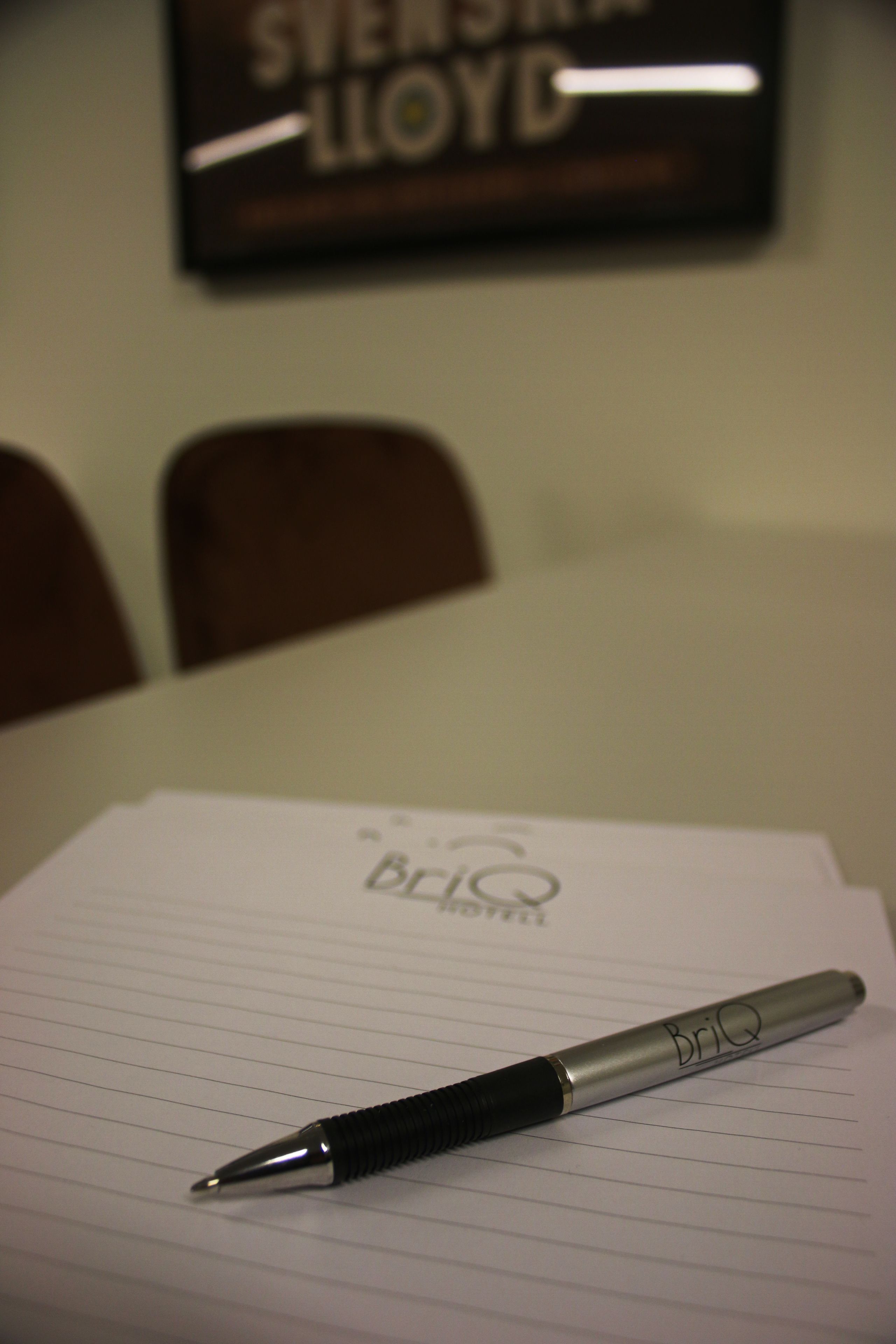 Een pen op ruitjes papier, een logo, een bordje in een lijst en twee stoelen op de achtergrond.