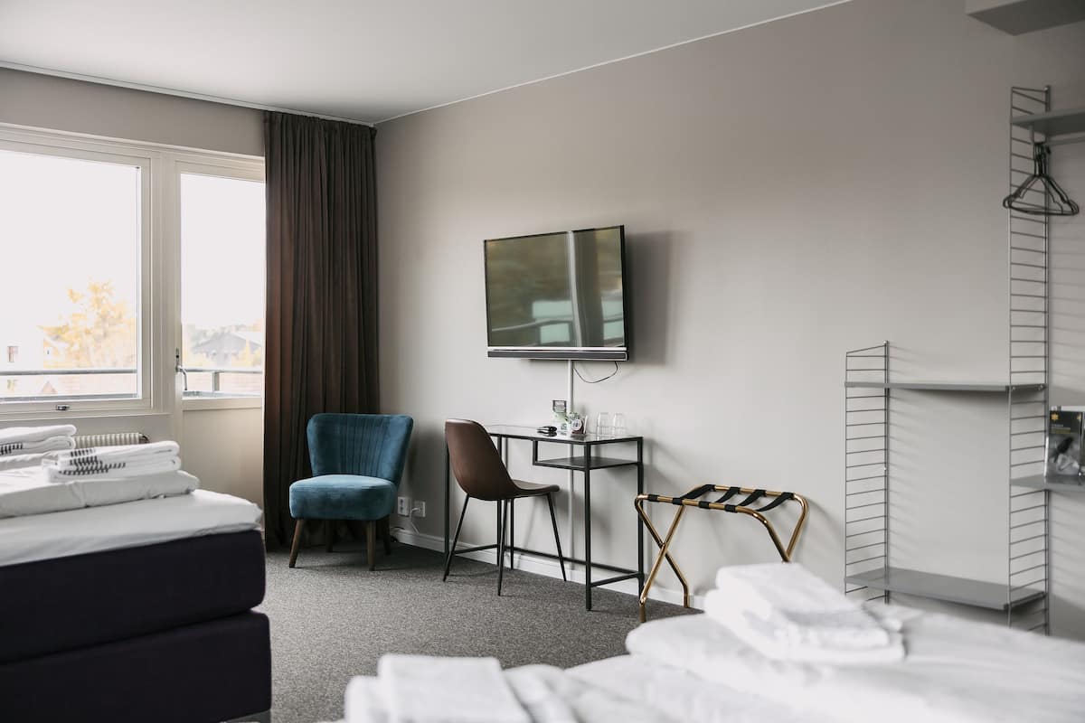 A hotel room with a bed, a desk, a chair, a TV, and a window with curtains.