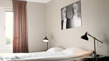 A hotel room with a bed, two bedside lamps, a chair, a window with curtains, and a wall-mounted picture.