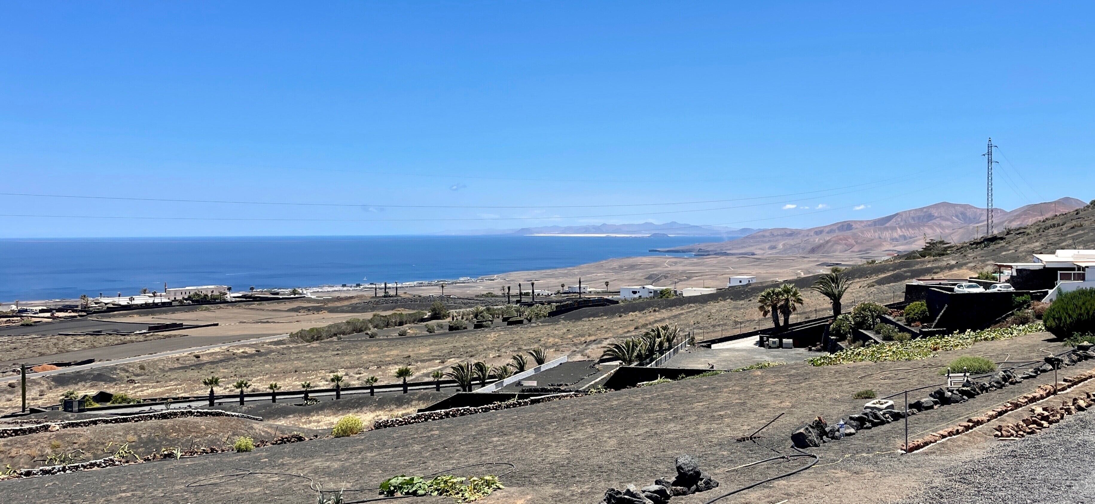 A coastal landscape with a clear view of the sea, a few buildings, and a distant mountain range.