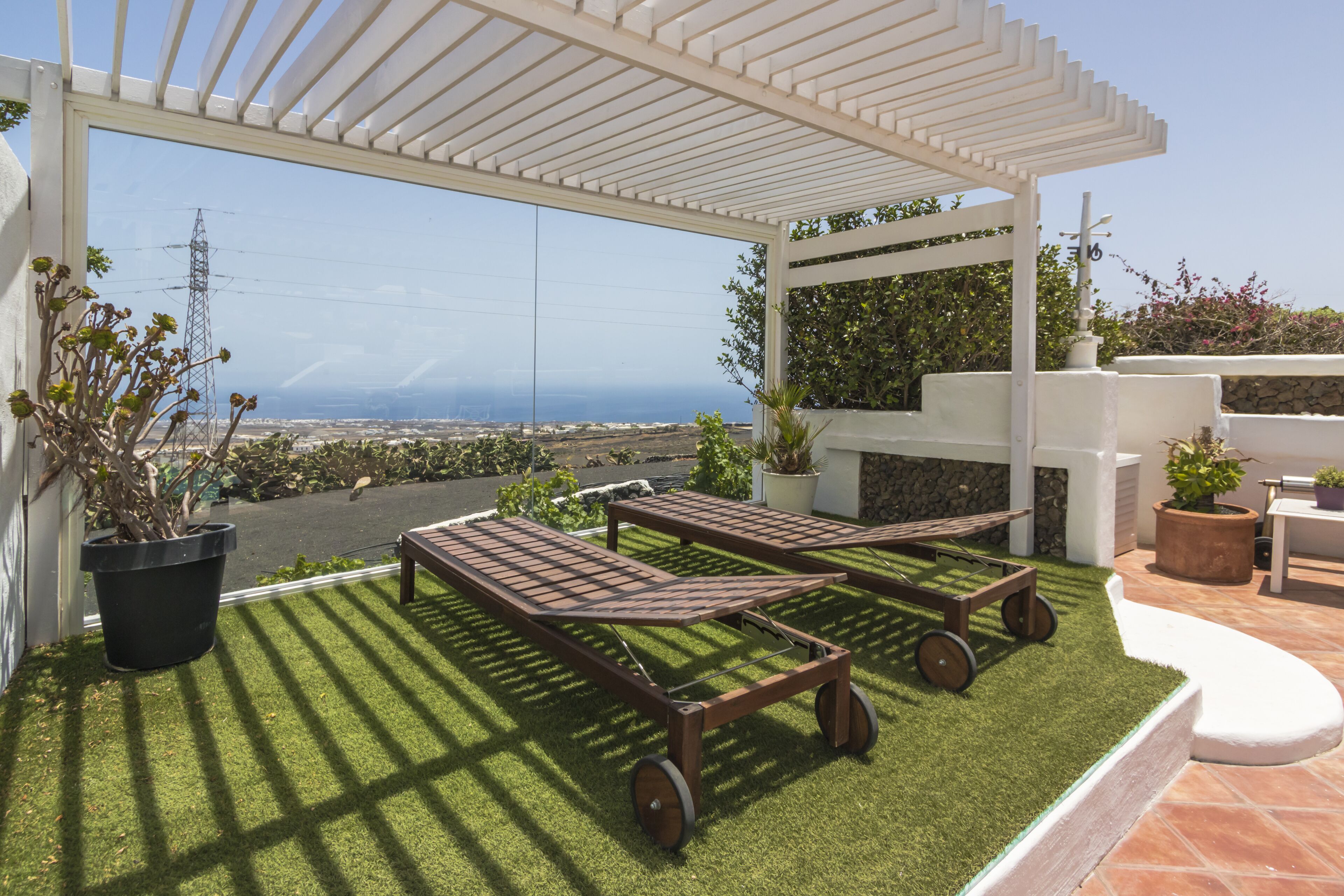Une terrasse avec deux chaises longues, une pergola et une vue sur la mer.