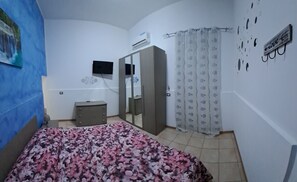 A bedroom with a bed, a wardrobe, a TV, and a wall-mounted air conditioner.