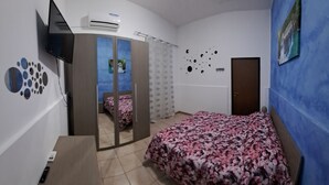 Ein Schlafzimmer mit einem Bett, einem Fernseher, einer Klimaanlage, einer Tür und einem Spiegel.