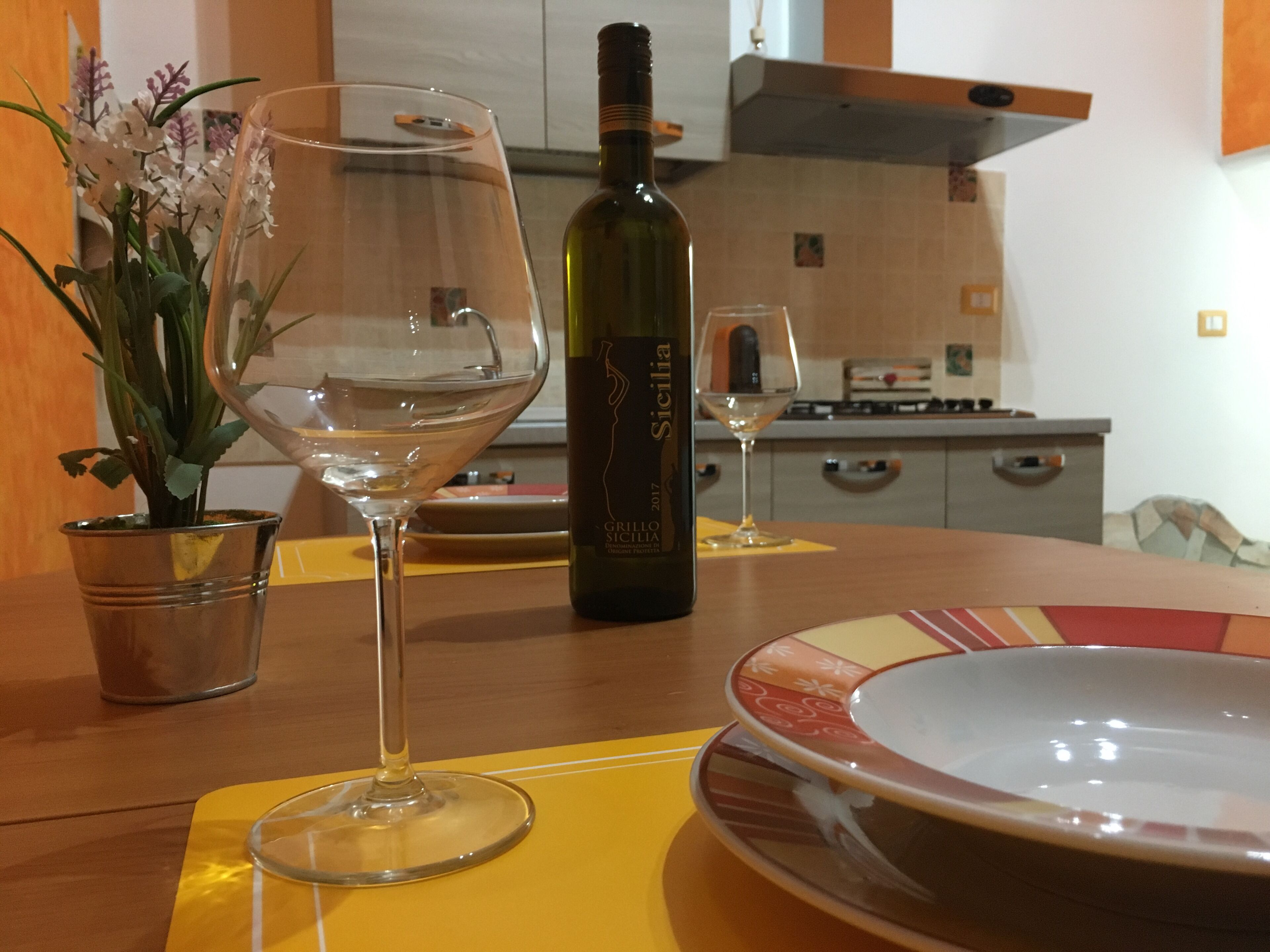 Un tavolo da pranzo con una bottiglia di vino, due bicchieri da vino, una ciotola e una pianta in vaso.