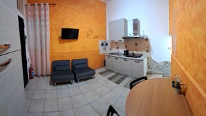 Ein kompaktes Zimmer mit Küchenzeile, zwei Sofas, einem Esstisch und einem an der Wand befestigten Fernseher.