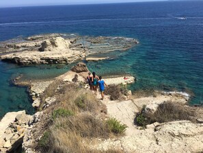 A rocky coastal area with clear blue waters and a small boat in the distance.