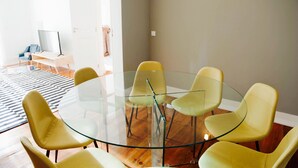 Una sala de estar moderna con una mesa de vidrio rodeada por sillas amarillas, un televisor sobre un mueble bajo y un tapete a rayas en el suelo.