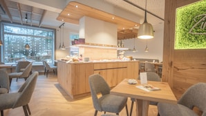 A modern cafe with wooden furniture, a central counter, and pendant lighting. - Hotel dasZimmermann (Todtmoos)