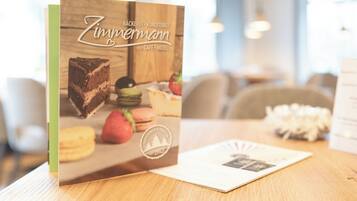 Un menu ou une brochure intitulée « Zimmermann », comportant une image de dessert, est posé sur une table en bois dans un café ou un hôtel.