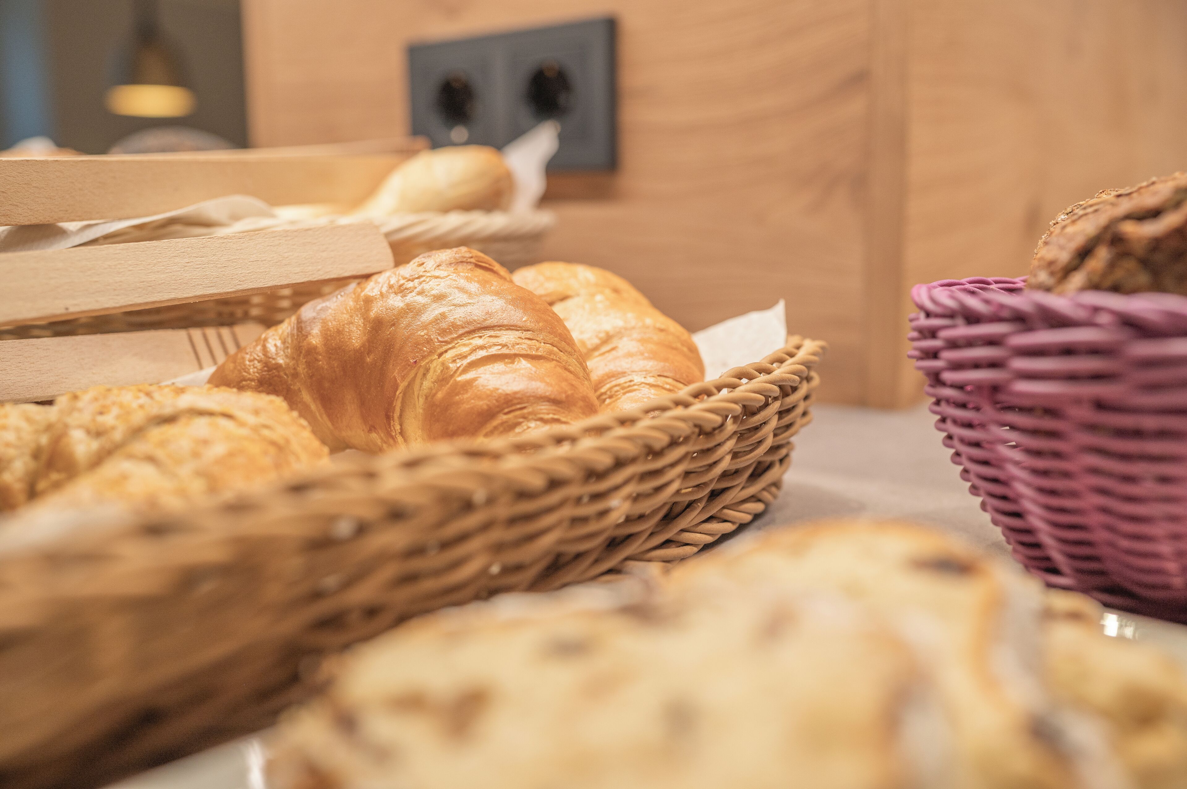 A variety of breads and pastries displayed in wicker baskets on a wooden table.