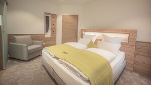 A bedroom with a large bed, a chair, a nightstand, and a wooden headboard. - Hotel dasZimmermann (Todtmoos)