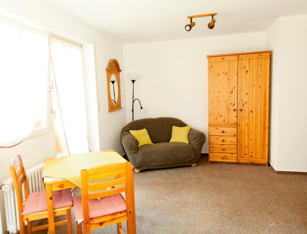 A room with a wooden table and chairs, a sofa, a wooden wardrobe, and a radiator.