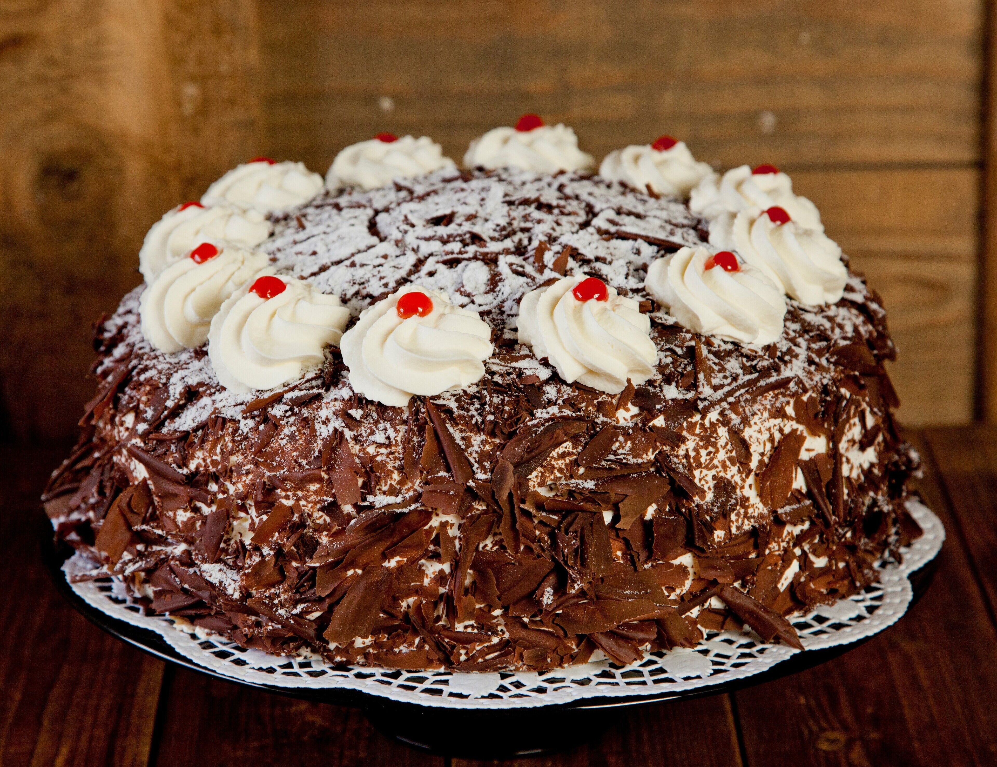 Bolo de chocolate com chantilly e cerejas sobre um bordado de renda.