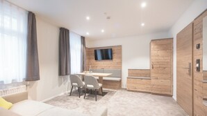 A modern room with a sofa, a dining table with chairs, a TV mounted on the wall, and wooden paneling on the walls. - Hotel dasZimmermann (Todtmoos)