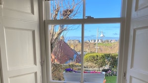 Asiento junto a la ventana con un cojín amarillo, un valance estampado y vistas de un paisaje costero con edificios y un faro.