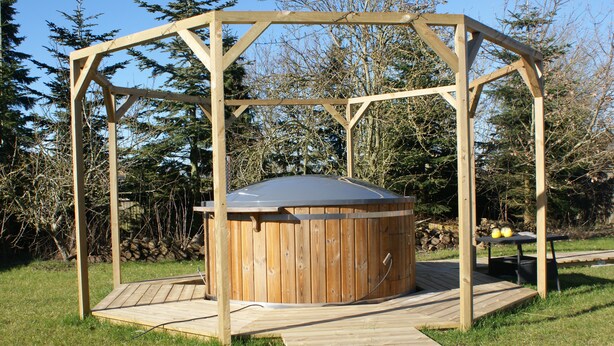 Een houten jacuzzi met een pergola, omringd door gras en bomen.