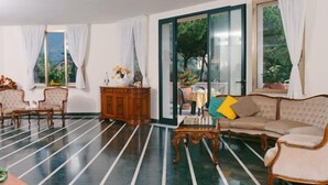 A spacious living room with a striped floor, a sofa, a chair, a wooden cabinet, and a table with a vase of flowers. - Hotel Da Filiè (Seravezza)