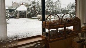 A view through a window of a snowy garden with a small gazebo, a wicker basket with magazines, and a table with glasses and plates. - Hotel Da Filiè (Seravezza)