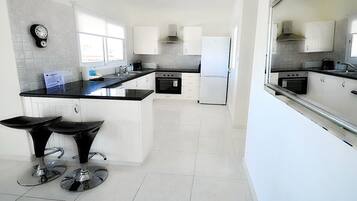 A modern kitchen with white cabinets, a black countertop, and a built-in oven. There are two bar stools with black seats.