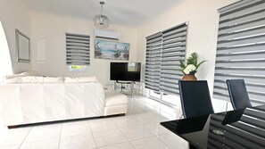 A modern living room with a sofa, TV, and a table with a laptop.