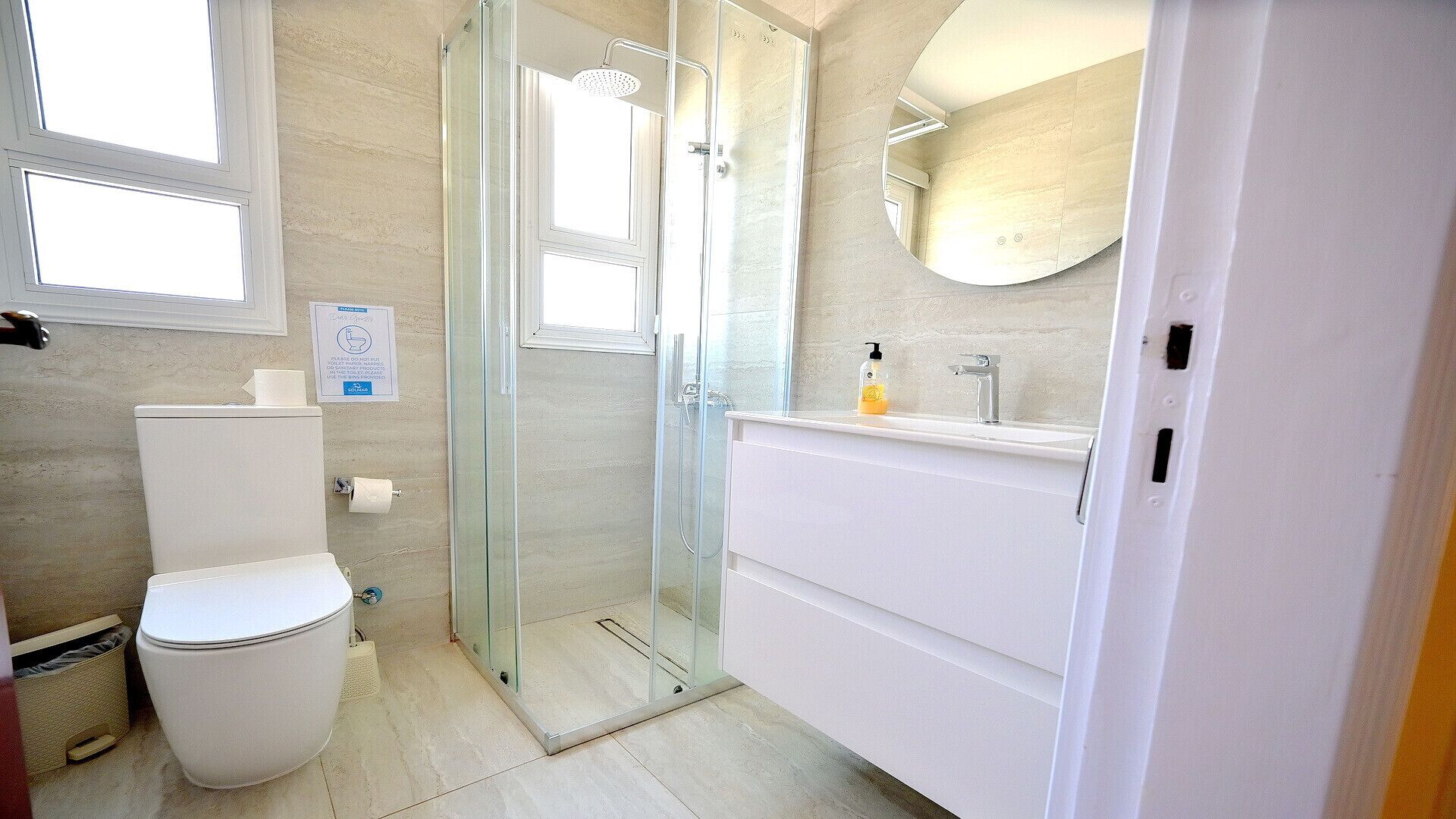 A bathroom with a toilet, a glass-enclosed shower, and a white vanity with a mirror.