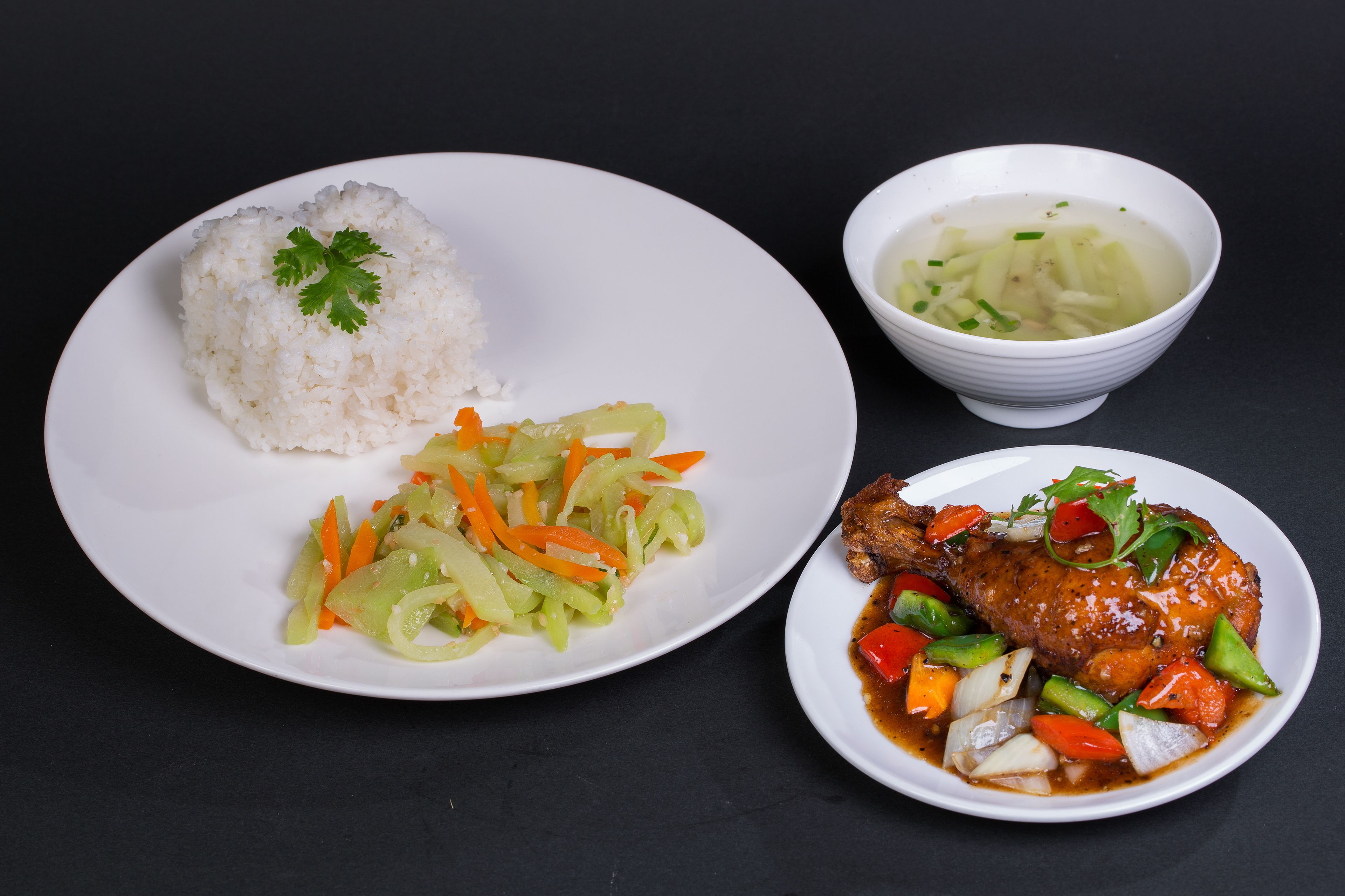 Un plato de arroz blanco con guarnición, un tazón de sopa y un plato con carne y verduras.