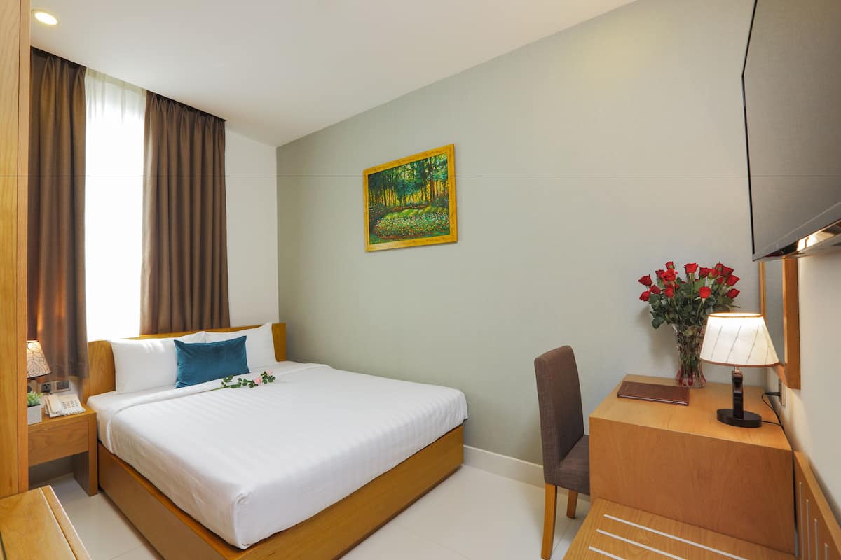 Une chambre d’hôtel avec un lit, un bureau doté d’une lampe, une chaise, un vase avec des fleurs et un tableau au mur.